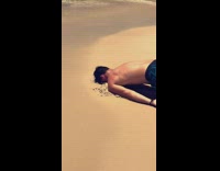 Guy does the worm in sand at the beach, goes into water