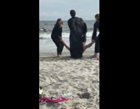 People in robes carry guy into water 