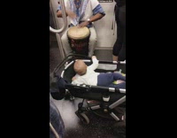 Man in blue daishiki plays bongo drums for baby in carriage stroller on subway train