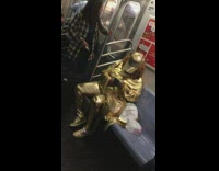 Woman dressed in all gold clothing sits on subway train and texts on her phone