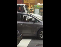 Man plays yellow maracas in grey mini van while waiting at a stop light
