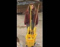 Collab KaleSaladIG - Woman red jacket stands and stares at mop bucket in warehouse with barrels