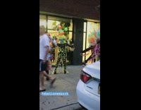 Human art with colorful pointy shapes dance on sidewalk, woman laughs and snorts