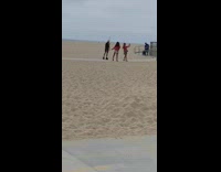 Girl pink jacket wave behind friend beach
