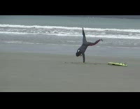 Surfer in wetsuit dances and cartwheels on the beach green surfboard