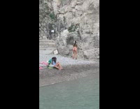 Lady in brown bikini records dance on beach rocks 