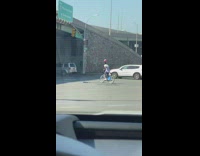 Man in blue bike with basketball on head rides in street