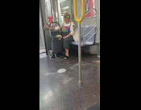 Woman wears rainbow visor covering face and polaroid shirt on subway train