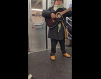 Man plays guitar and panpipes inside train