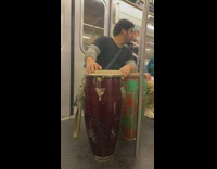 Man plays tall red and green drums on train