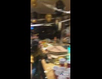 Orange cat jumps from tall cabinet onto kitchen counter, friends clap at party