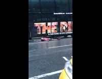 Guy in red shirt lays on street in the rain and blocks traffic