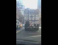 black suit case hanging off ladder of brown trash truck