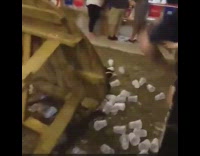 Stripe shirt guy and blue shirt guy knock over tower of clear cups on round wooden table