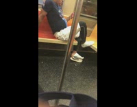 Man sits criss cross with shoes off and on seats on subway train