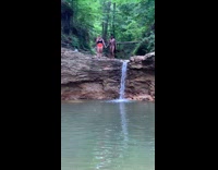 Two girls get ready to jump into water one slips