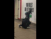 Person wearing alien masks and bird feather costume dancing in station