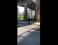 Guy gives haircut on sidewalk under bridge 