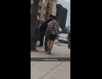guy in tank top walks along sidewalk with surf board 