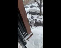 Girl watches guy laying on snow sidewalk 