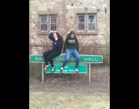 Two girls sit on sign and fall back over into bush