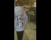 A couple walks down street with spacesuit teddy bear on their backs