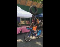 Guy balances tire on his head while riding bike