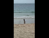 Woman in yellow bikini kneel and poses in front of tripod at the beach