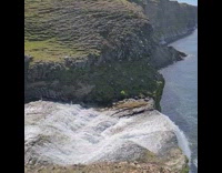 Large waterfall flows over brown rocks grass