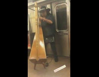 Man in black wide brim hat plays the harp on the subway train