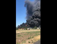 Black cloud of smoke in the sky after  building catches on fire across field