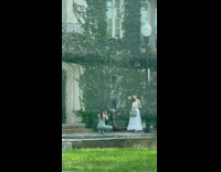 Woman in white dress poses near the building with vines
