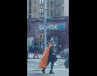 Man Wears Orange Cape while Crossing Street 