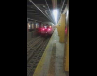 Two people riding on the outside back of a subway train departing 
