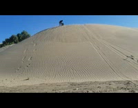 Guy slides down sand dune on sled