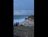 Woman black dress raises hands on beach
