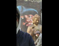 Guy standing by mural sees buddha statue 