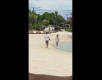 Brown shirt blue shorts guy walks beach 