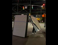 Two people carry large mattress on street