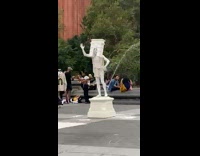 Guy stand covered in white paint wearing New York arch on head 
