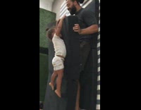 Little girl lays on black couch cushion as dad shakes cushion on the floor