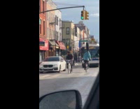 Guy rides bicycle with tire on head 