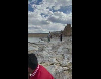 Man in gray short and a beanie tiktok dance at the beach rocks