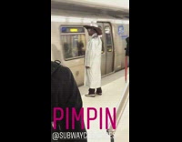 Man in metallic silver coat hat and sunglasses waits for train to stop at subway station