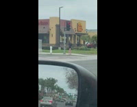 Woman takes selfies in front of el pollo loco on street corner