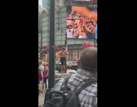Shirtless man plays flute in black shorts and thrusts hips while standing on cement block in new york city