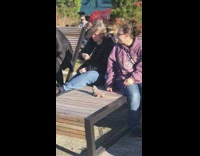 Lizard on leash sits on patio chair next to woman in purple jacket