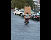 Woman holds large box while on motorcycle 