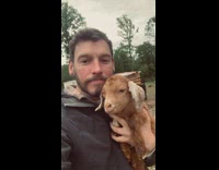 Guy snuggles with brown baby goat in his arms named Rosie 
