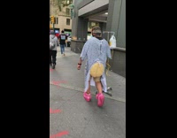 Guy walks down sidewalk in pink shoes and hospital gown 